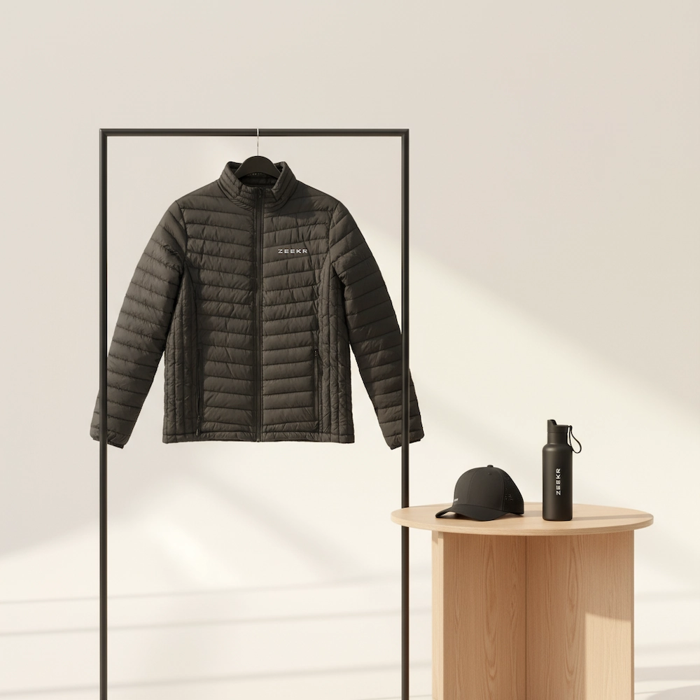 En kviltad Zeekr-jacka på en klädställning, med en svart Zeekr-keps och vattenflaska på ett litet träbord.